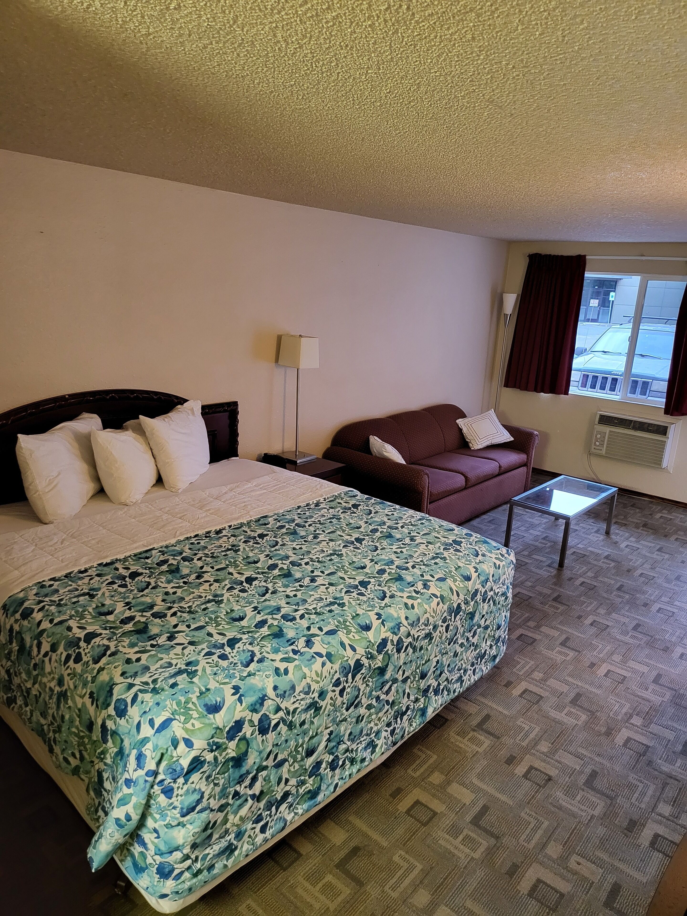 Ein Hotelzimmer mit einem großen Bett, einer Couch, einem kleinen Tisch und einem Fenster mit Vorhängen.