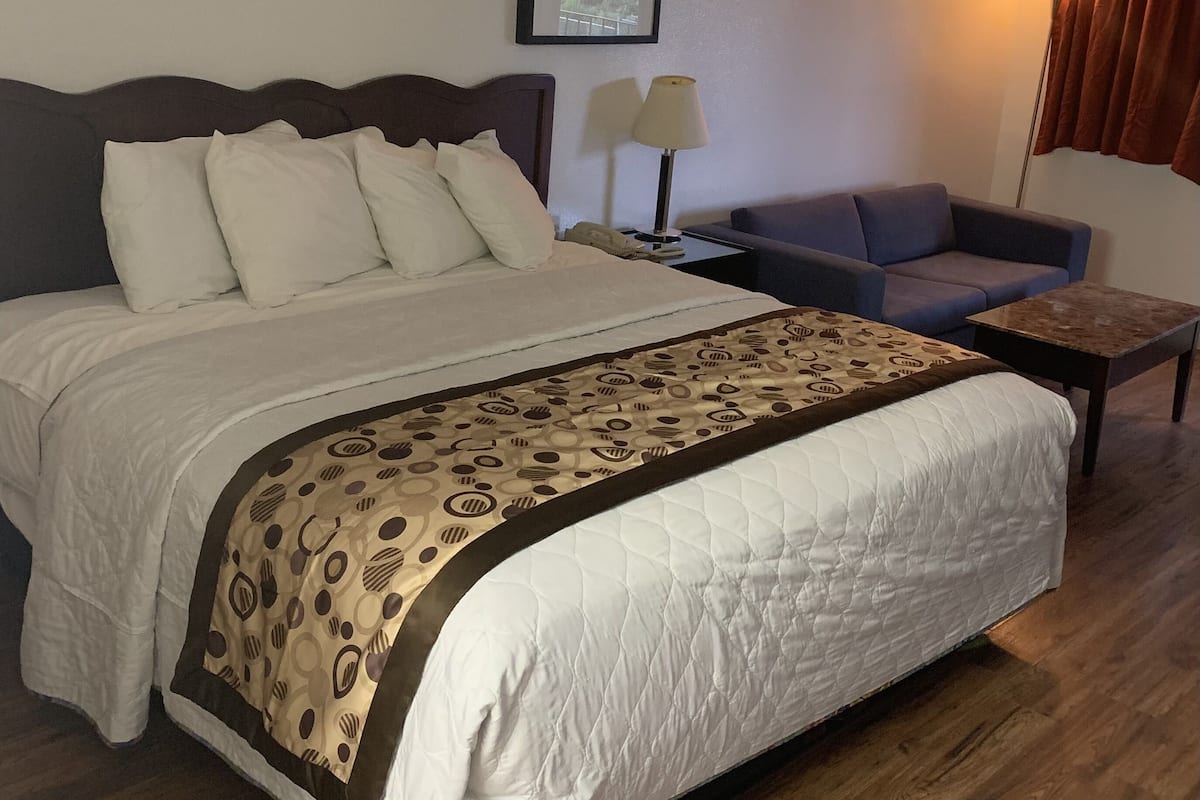 A hotel room with a large bed, a sofa, a small table, a lamp, and a framed picture on the wall.