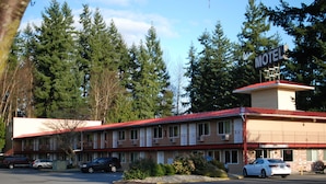 A motel with a red roof and a sign indicating it is a motel. There are several cars parked in front, and the building is surrounded by trees.