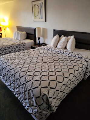 A hotel room with two beds, each with a patterned bedspread, a nightstand with a lamp, and a framed artwork on the wall. - Smokey Point Motor Inn (Arlington)