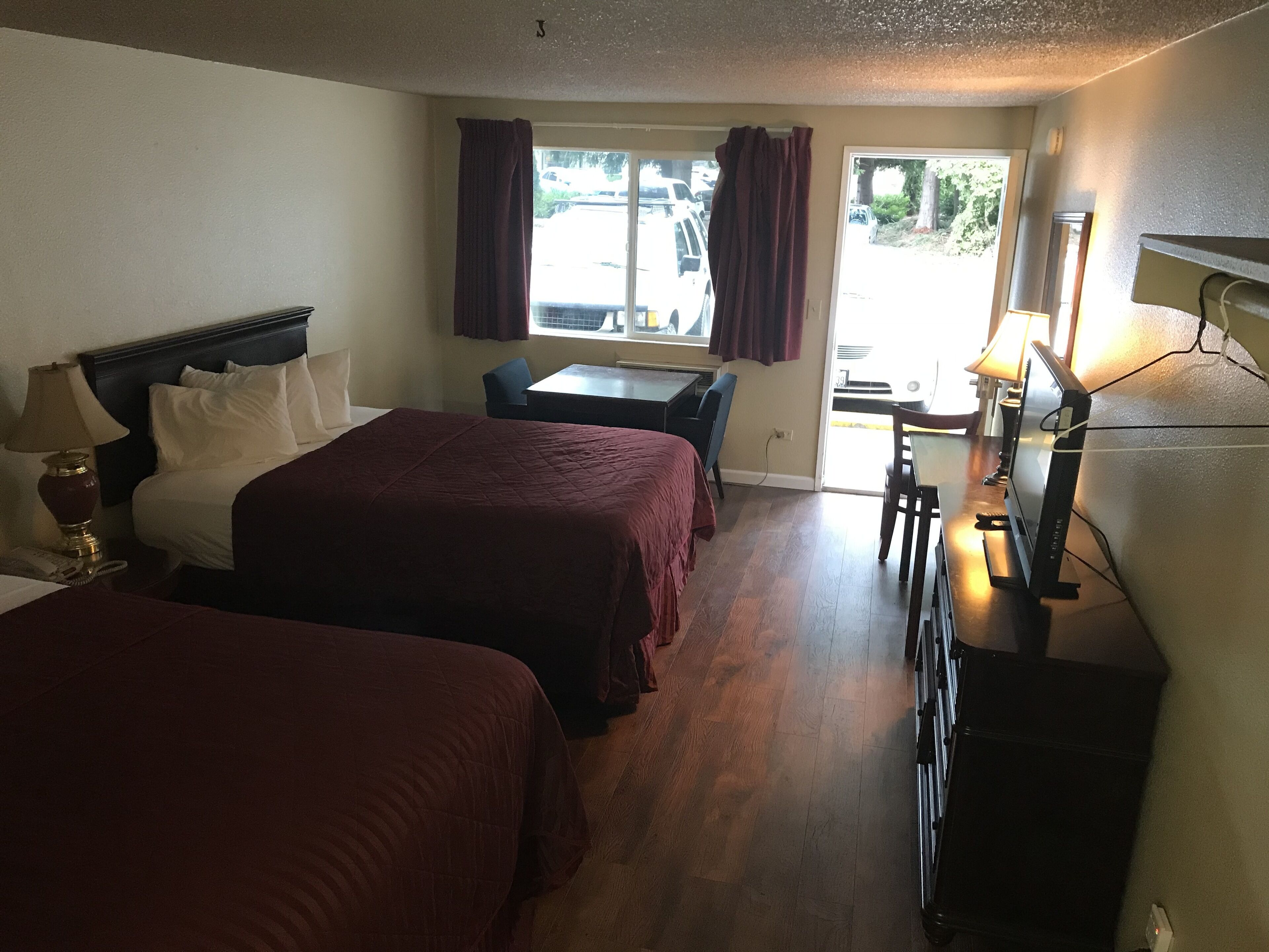 A hotel room with two beds, a desk, a chair, a TV, and a window with curtains.