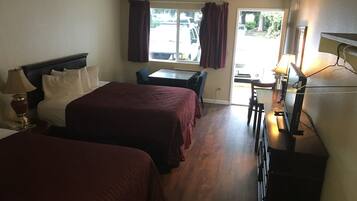 A hotel room with two beds, a desk, a chair, a TV, and a window with curtains.