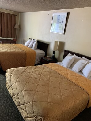 A hotel room with two beds, a nightstand, a lamp, and a framed picture on the wall.