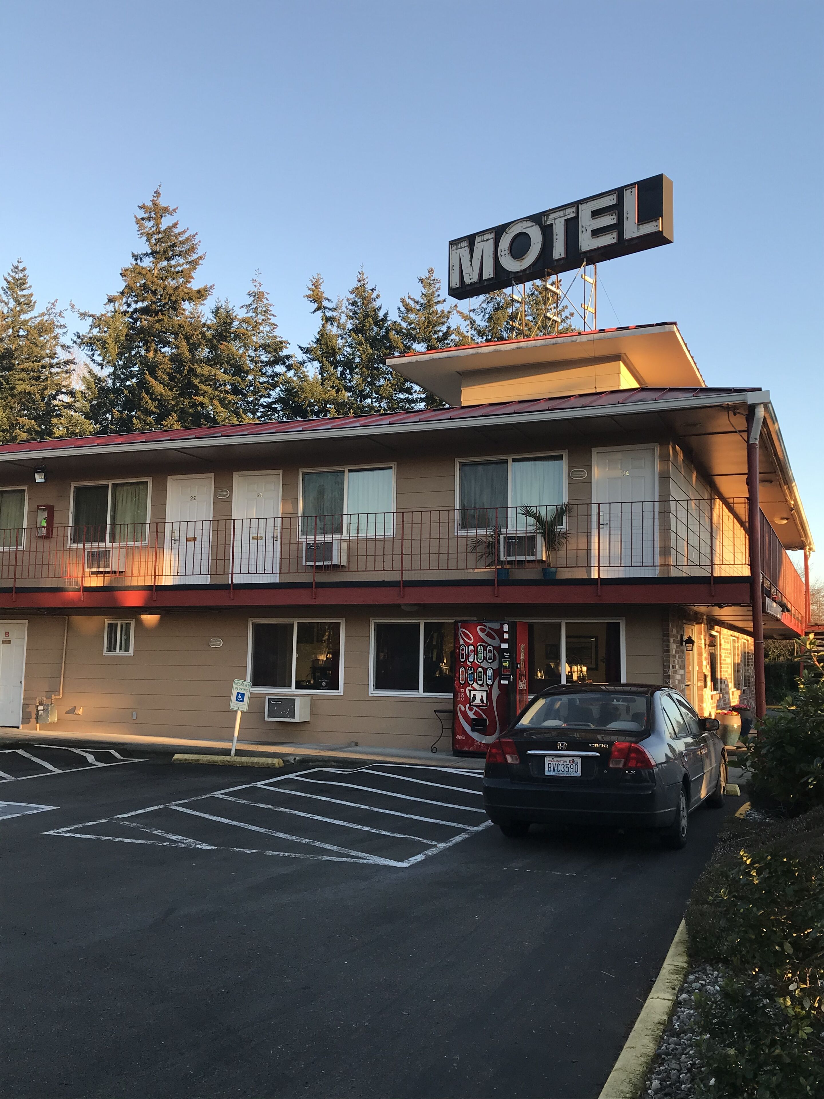 A motel with a signboard, parking lot, and a car parked in front.