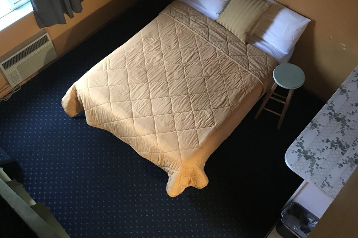 A hotel room with a bed, a small round table, a lamp, and a picture on the wall.