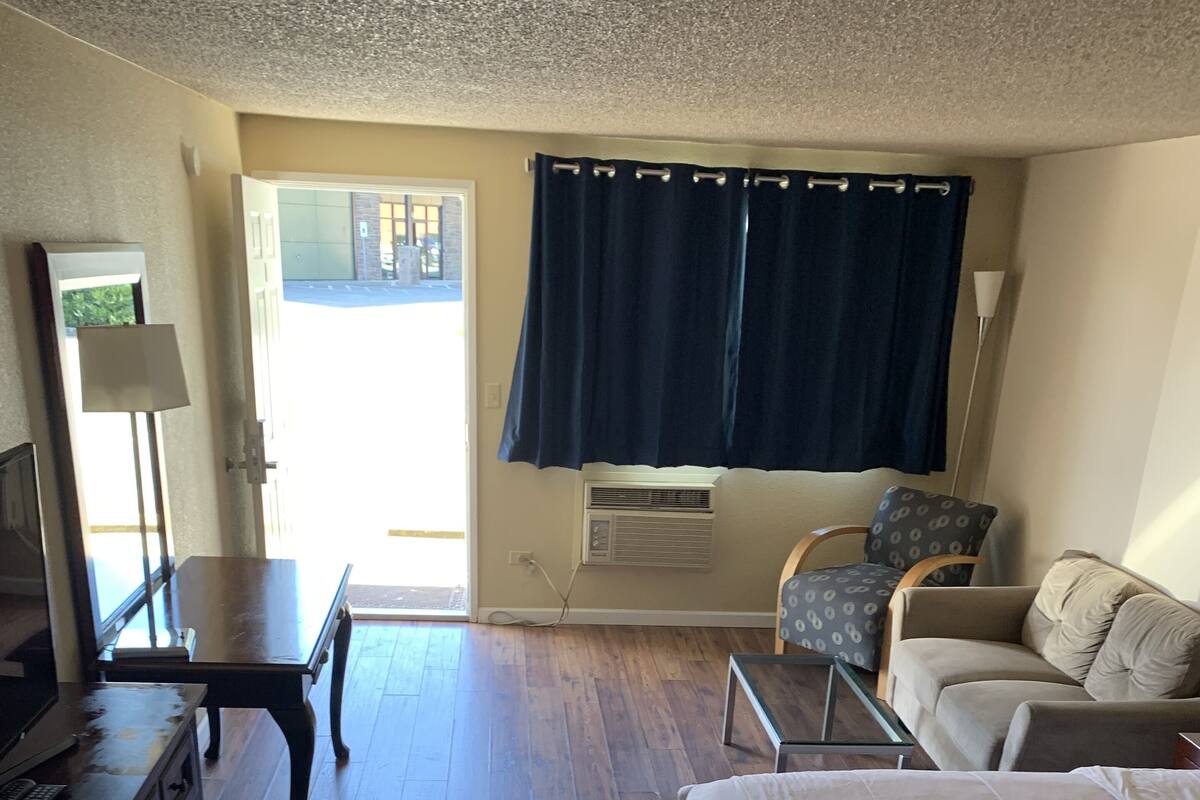 A hotel room with a large bed, a desk, a chair, a dresser, and a window with curtains.
