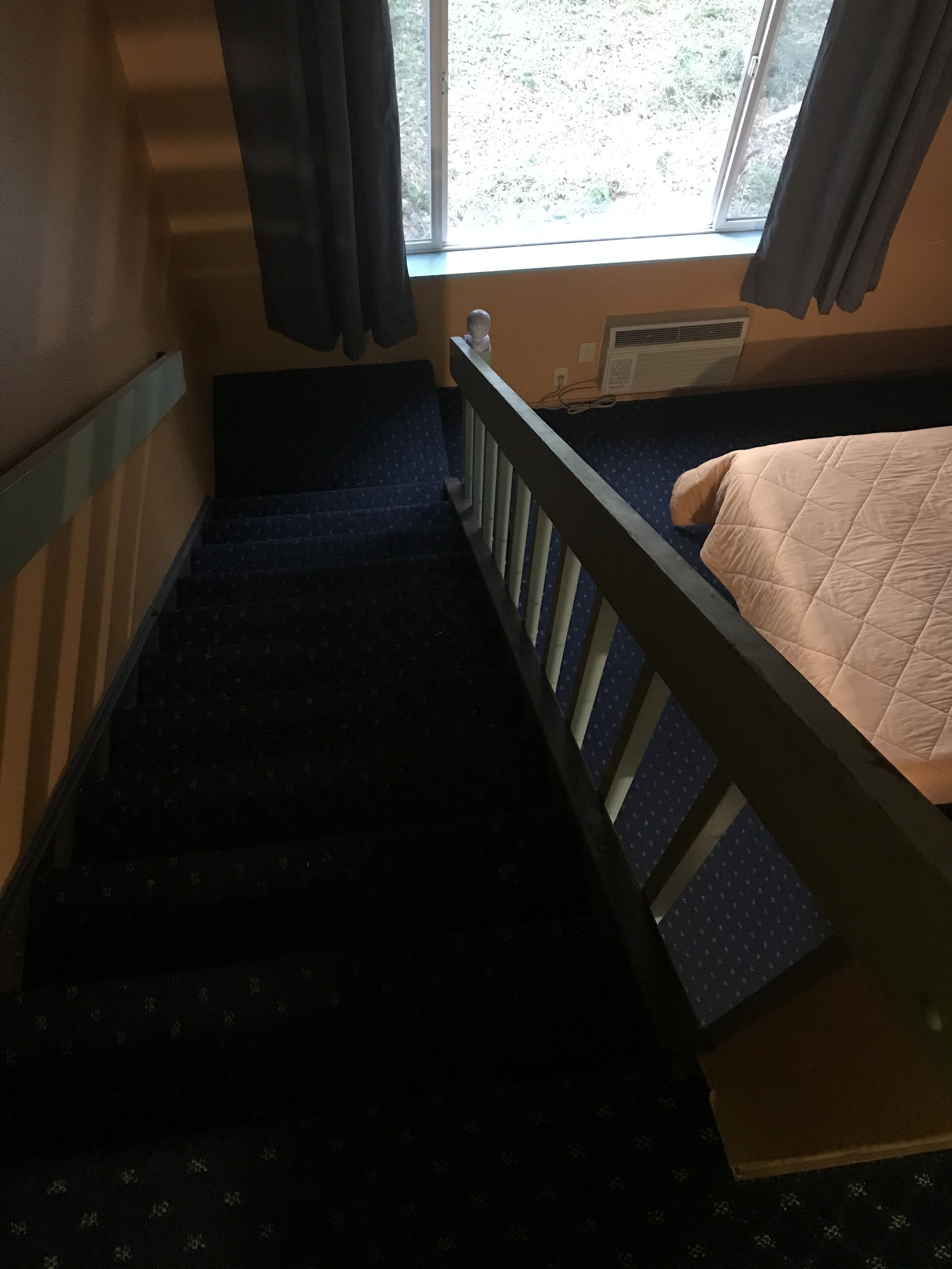 A room with a bunk bed, a window with curtains, a radiator, and a staircase.
