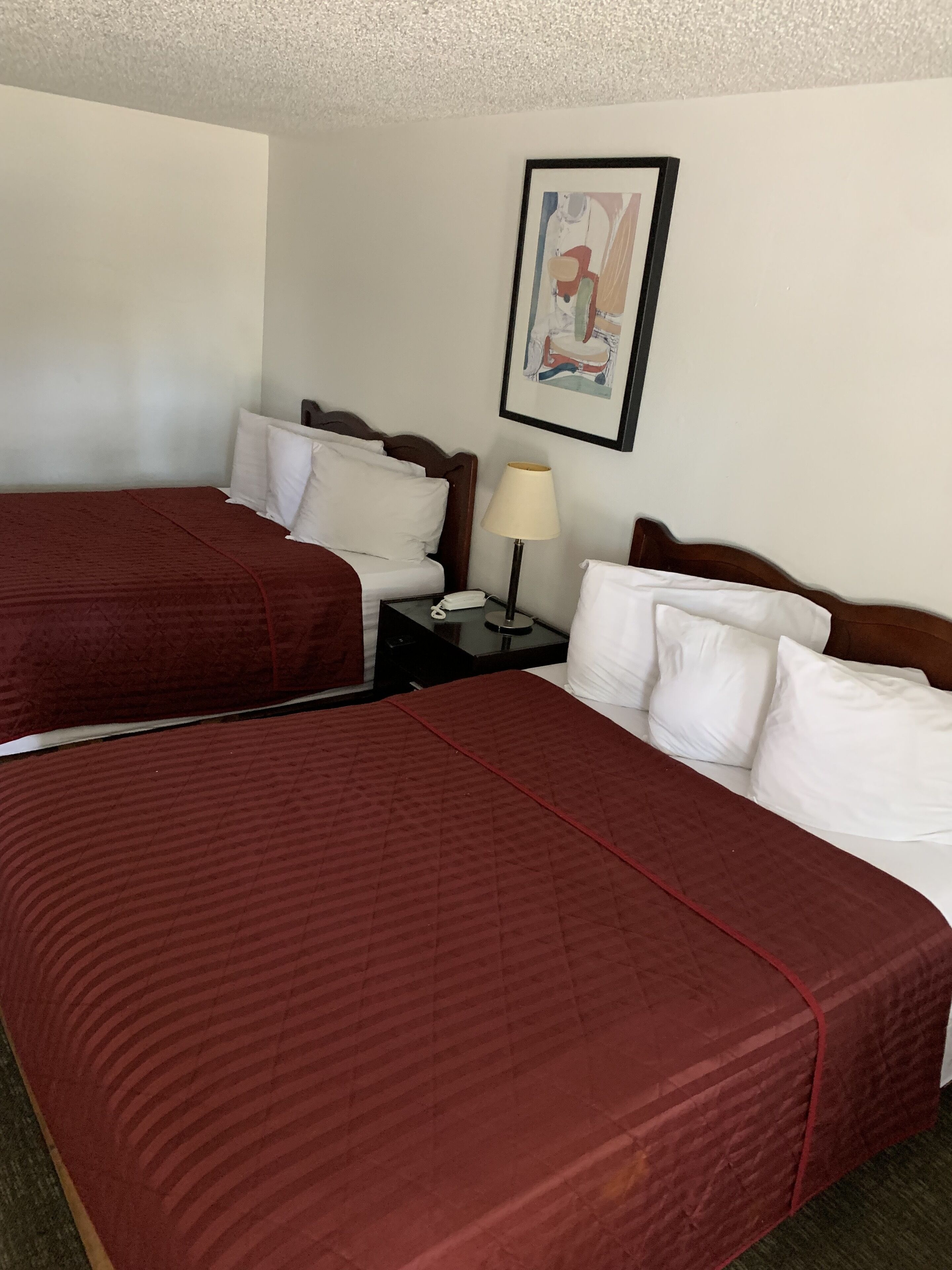 Une chambre d’hôtel avec deux lits, chacun recouvert d’une couverture rouge, agrémenté d’oreillers blancs et doté d’une table de chevet avec une lampe.