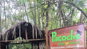 Een houten pad dat leidt naar een rustiek onderkomen met een bordje voor Pacoche Lodge Reserve.