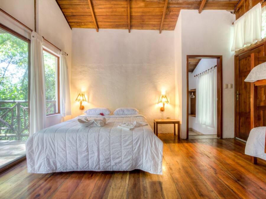 A spacious bedroom with a large bed, wooden flooring, and two wall-mounted lamps.