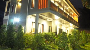 Une maison moderne à deux étages, dotée d’un balcon et éclairée par des luminaires extérieurs.