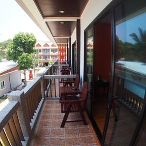 Een balkon met buitenmeubilair, uitzicht op een gebouw met meerdere ramen en een betegelde vloer.