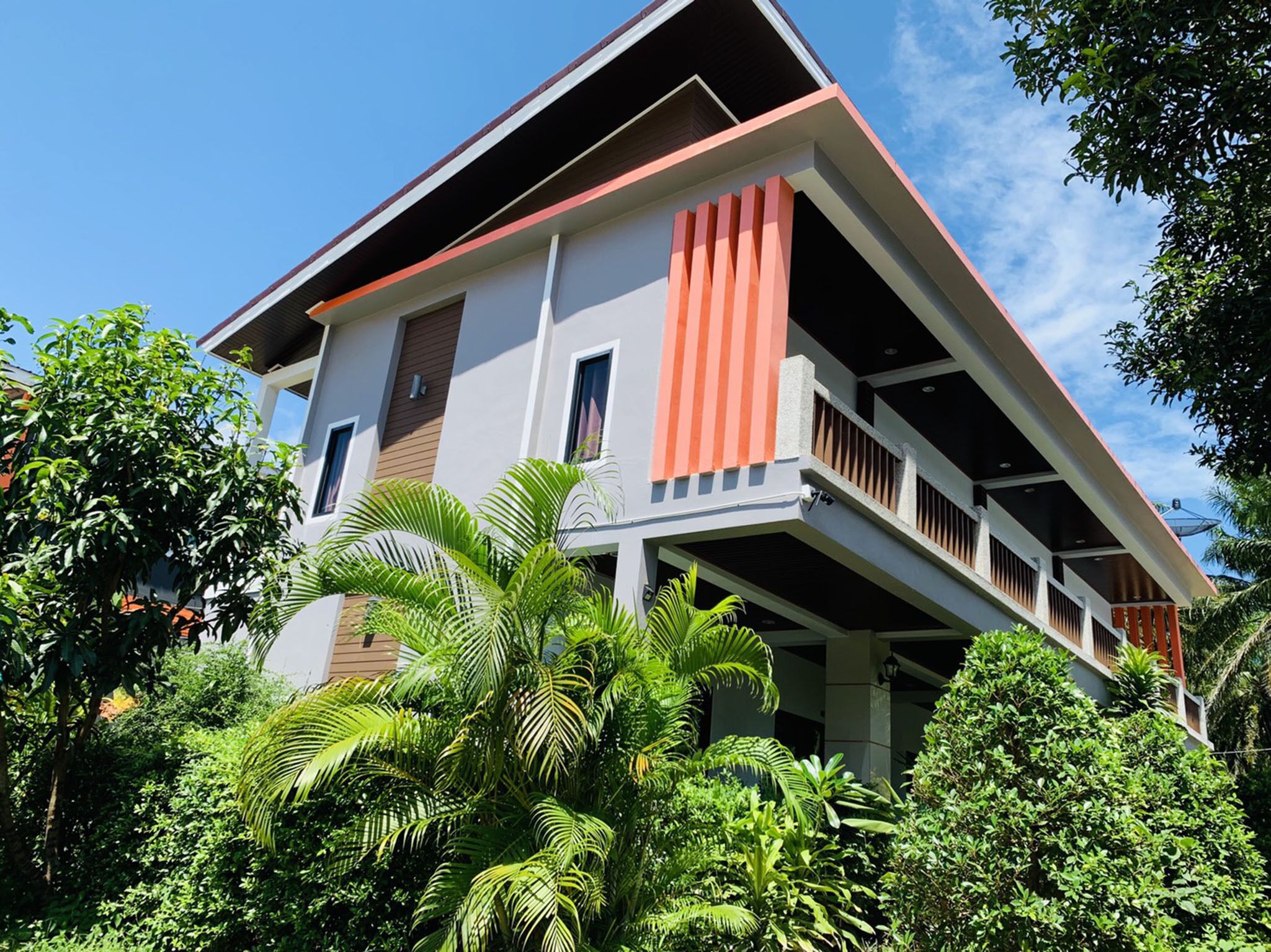 A two-story house with a balcony, surrounded by lush greenery.