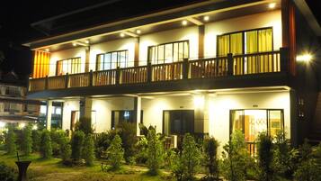 A two-story hotel with a balcony on the upper floor, multiple windows, and a well-lit entrance.