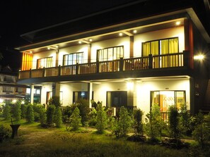 Een hotel met twee verdiepingen, voorzien van een balkon op de bovenverdieping, meerdere ramen en een goed verlichte entree.