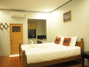 Een slaapkamer met een houten bed, wit beddengoed, een wandairconditioner, een lijst met bloemen erin en een deur met een decoratieve spiegel.