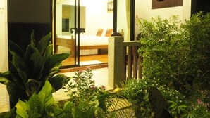 Une pièce bien éclairée, avec un lit, une porte vitrée donnant sur une autre pièce et un petit balcon agrémenté de plantes.