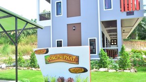 Une enseigne indiquant « Pongphipat Mansion », avec un bâtiment moderne en arrière-plan.