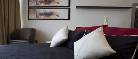 Habitación de hotel con una cama, dos almohadas, una colcha roja y dos cuadros abstractos en la pared.