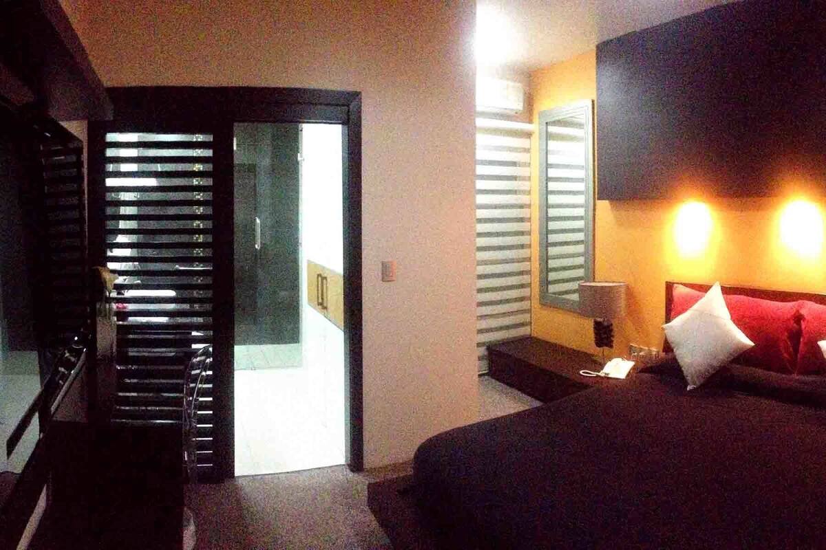 Una habitación de hotel con una cama, lámparas de noche, una puerta con persianas y una mesita.
