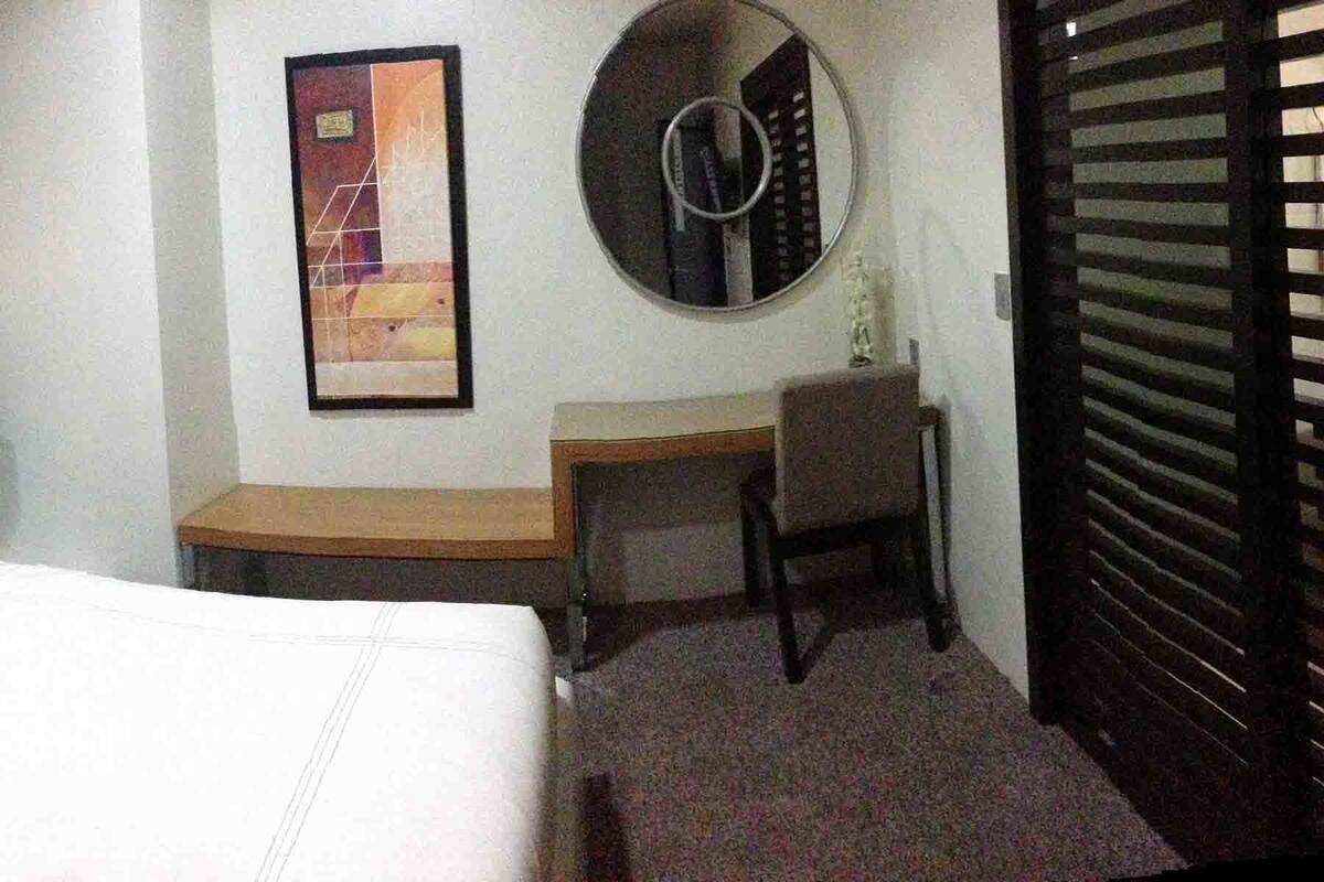 Una habitación de hotel con una cama, un escritorio, una silla y un espejo.