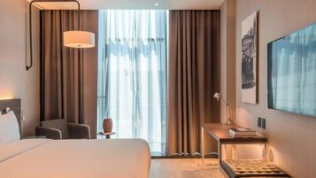 Una habitación de hotel con una cama grande, un escritorio con lámpara, una silla y un banco.