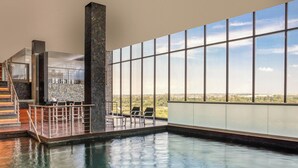Piscina interna com vista para a cidade, uma escadaria e um espaço de bar.