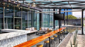 Uma área de bar moderna com balcão de mármore, assentos e uma televisão grande.