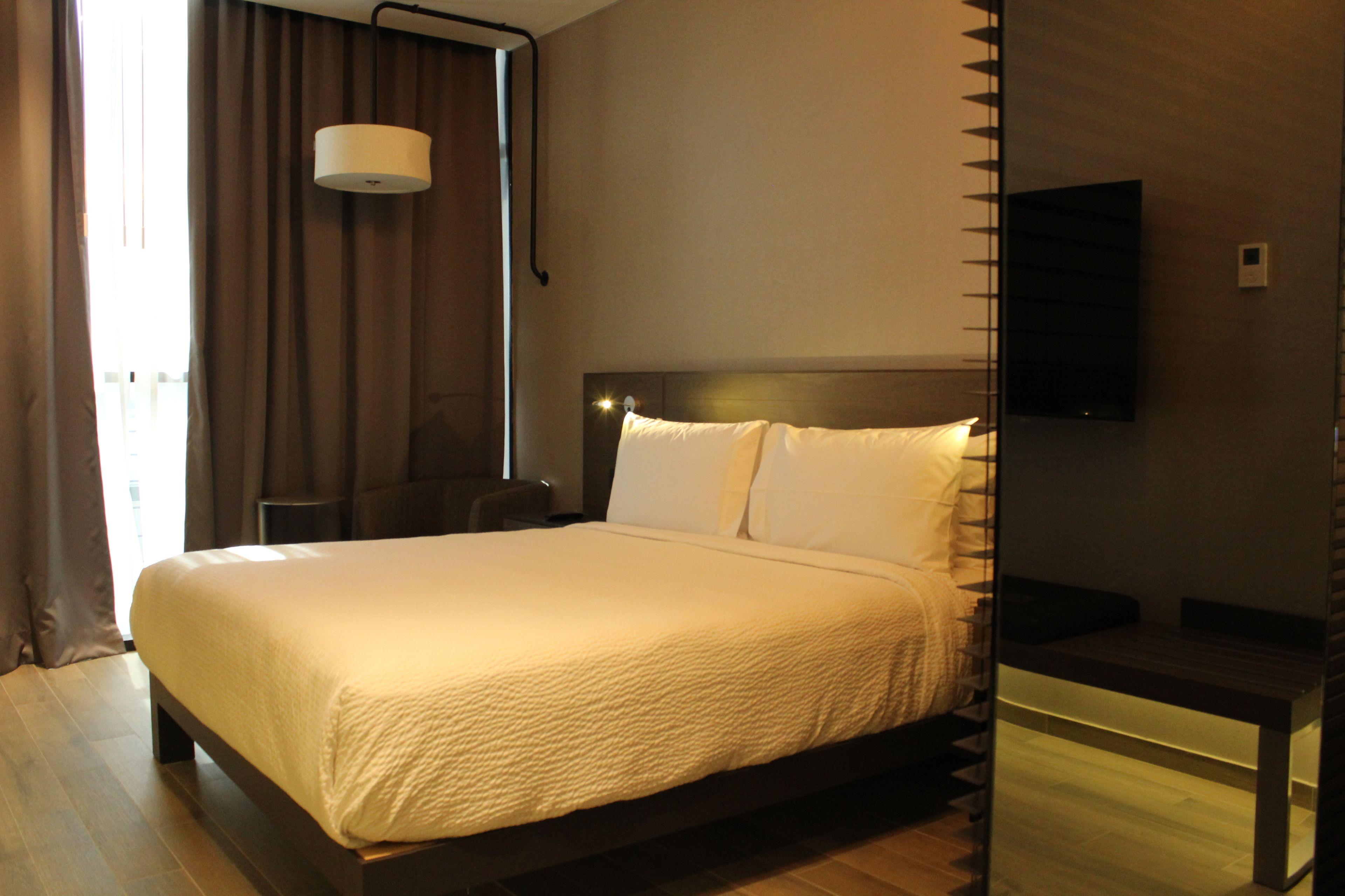 A modern hotel room with a large bed, a bedside table, a flat-screen TV, and a window with curtains.