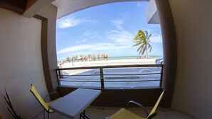 A balcony with a table and two chairs, overlooking a beach with palm trees and a clear sky. - Hotel & Suites Domani (Progreso)