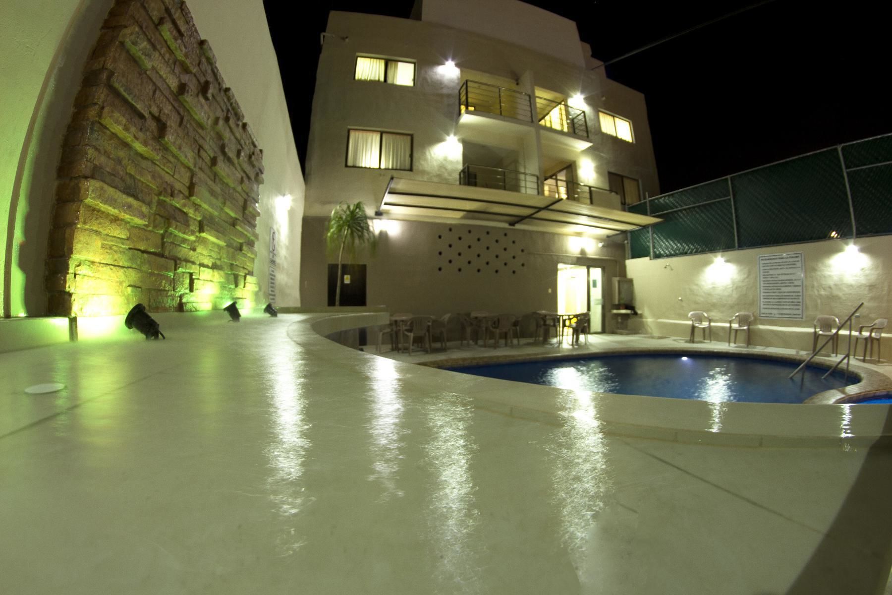 A nighttime swimming pool area with a building featuring multiple balconies and a poolside seating area.