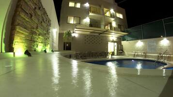 A nighttime swimming pool area with a building featuring multiple balconies and a poolside seating area.