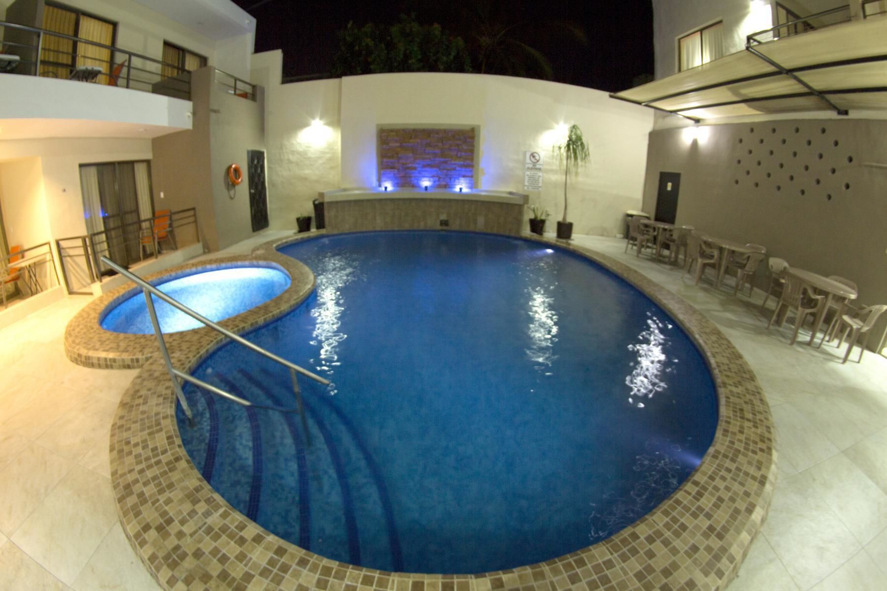Uma piscina com borda azulejada, rodeada por um alpendre com mobiliário de exterior.