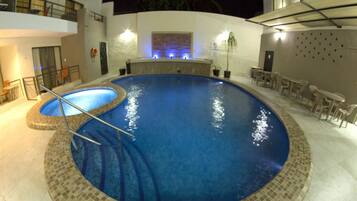 Uma piscina com borda azulejada, rodeada por um alpendre com mobiliário de exterior.