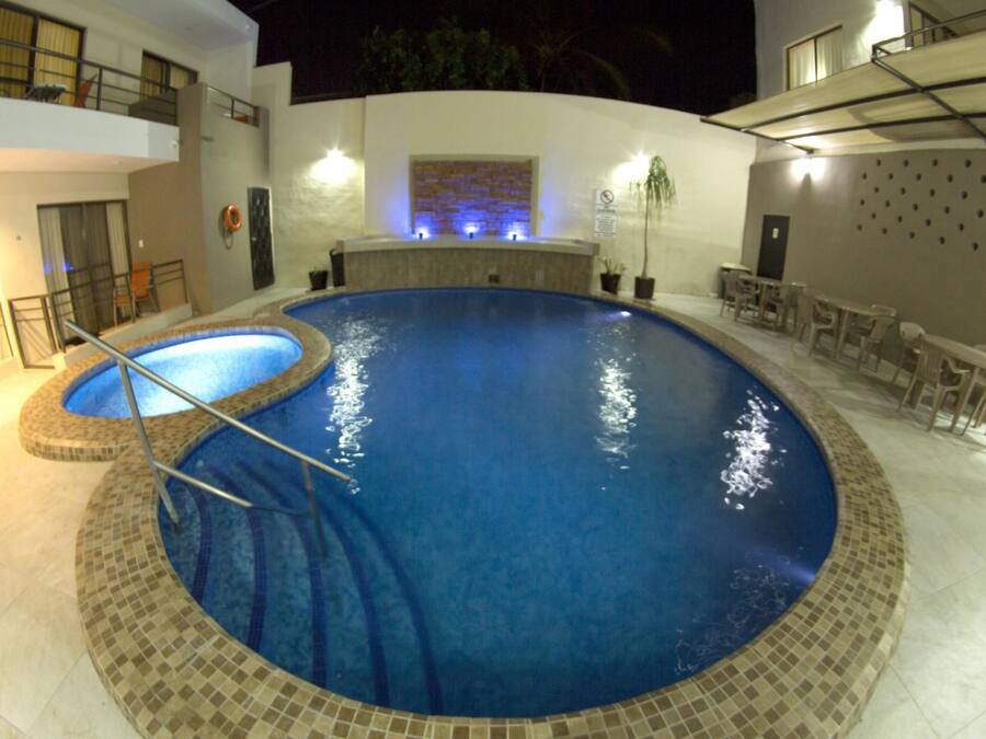 Uma piscina com borda azulejada, rodeada por um alpendre com mobiliário de exterior.