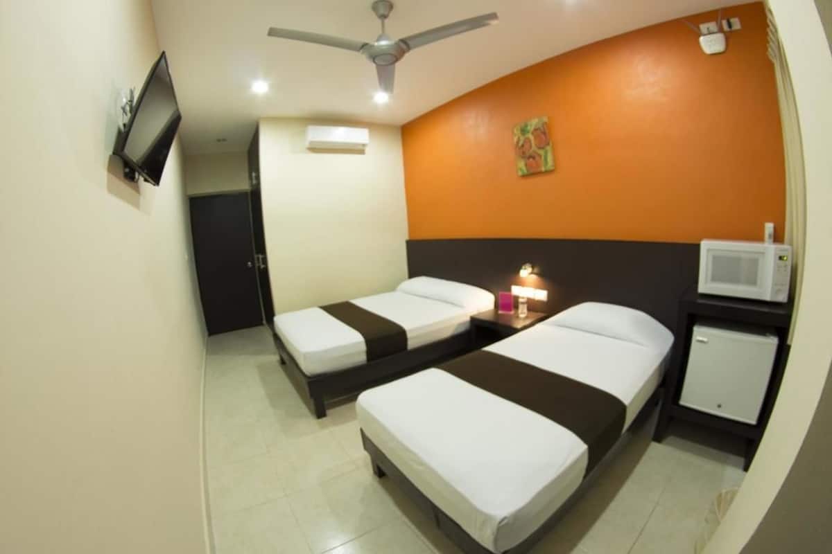 A hotel room with two single beds, a ceiling fan, a TV, a microwave, and a small cabinet.