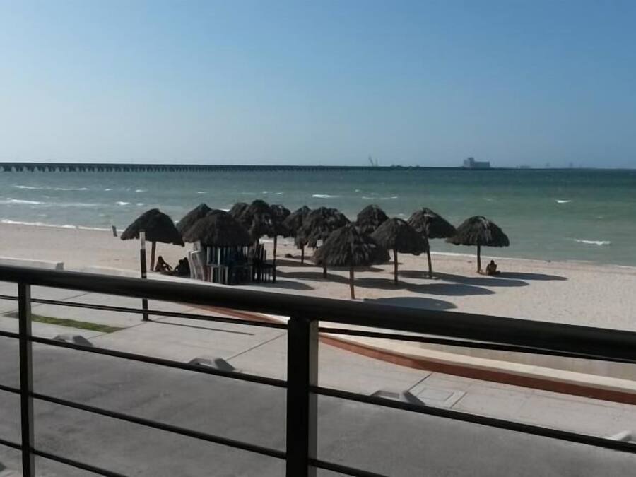 Une plage avec des parasols en chaume et une jetée en arrière-plan.