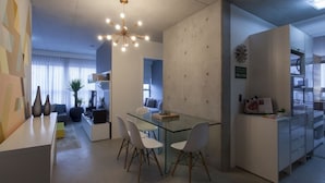Un salon moderne avec une table à manger en verre, des chaises blanches, un canapé et un luminaire suspendu au plafond.