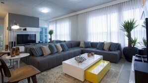 Un salon moderne avec un canapé d’angle gris, une table basse blanche et un téléviseur à écran plat.