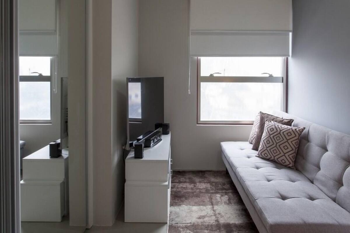 A modern bedroom with a large window, a sofa, a dresser, and a mirror.