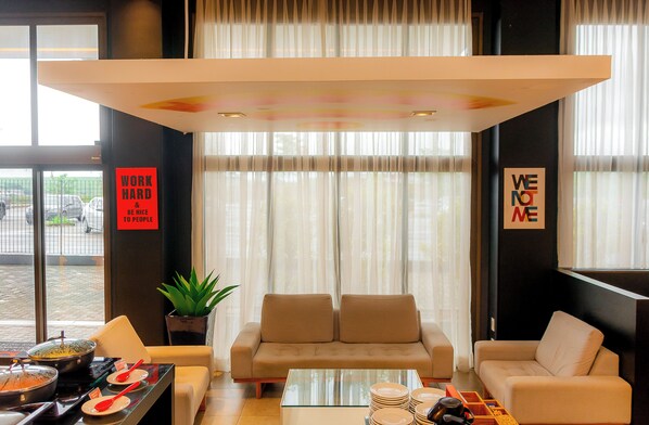 A modern hotel lobby with a sofa, a coffee table, and a dining area with plates and utensils. - Golden Tower Shopping by Fênix Hotéis (Pouso Alegre)