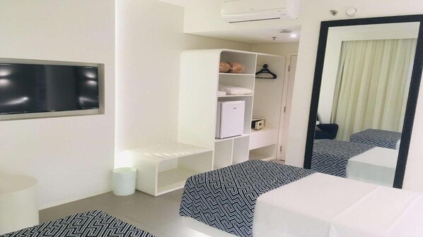 Habitación de hotel con cama, mesita de noche, armario, espejo y aire acondicionado.