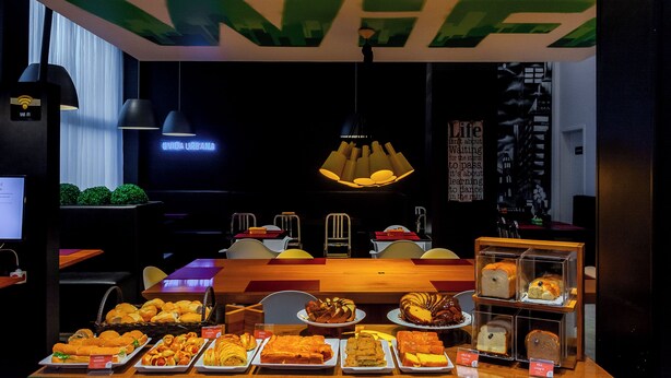 A restaurant with a wooden table and chairs, a neon sign, and various food items displayed. - Golden Tower Shopping by Fênix Hotéis (Pouso Alegre)