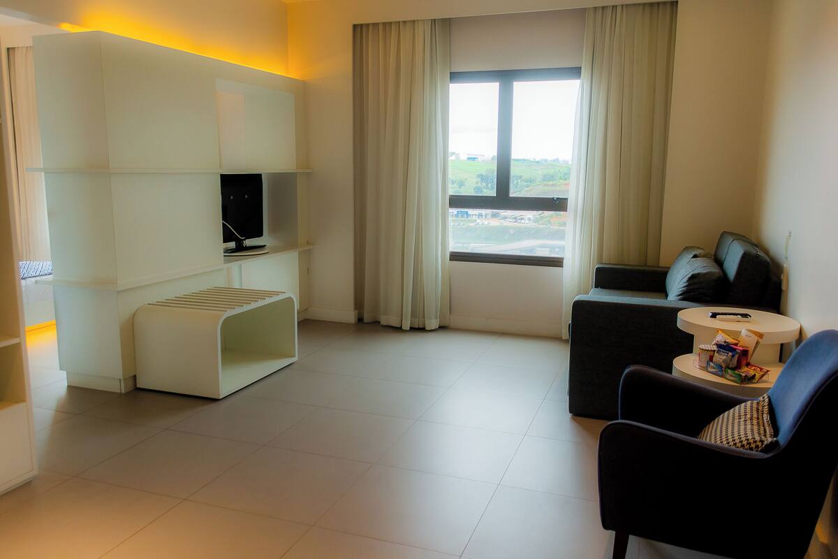Habitació d'hotel moderna amb televisió de pantalla plana, un sofà, una cadira, una taula petita i una finestra amb vista a la ciutat.