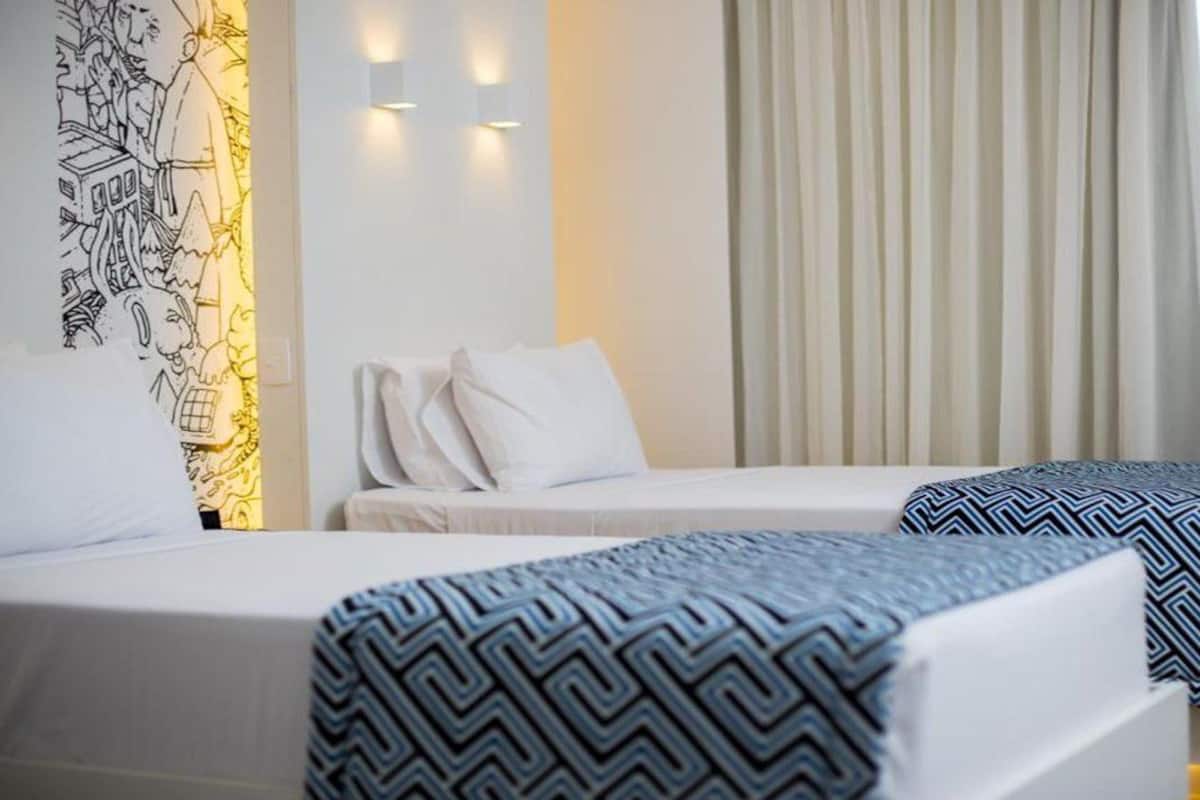 Una habitació d'hotel amb dos llits, un mural a la paret i una finestra gran amb cortines.