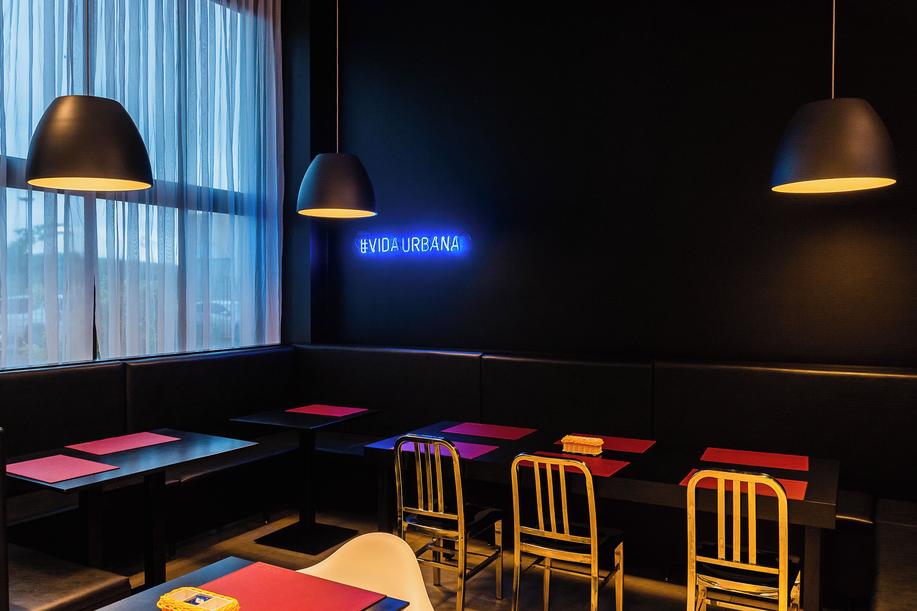 A restaurant interior with tables, chairs, and hanging pendant lights.