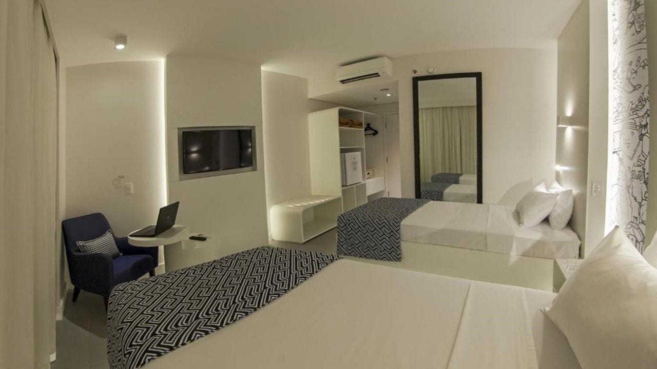 Een hotelkamer met twee bedden, een bureau met een laptop, een stoel, een kledingkast en een spiegel.