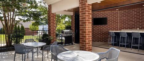 An outdoor patio with metal tables and chairs, a brick wall, and a barbecue grill.