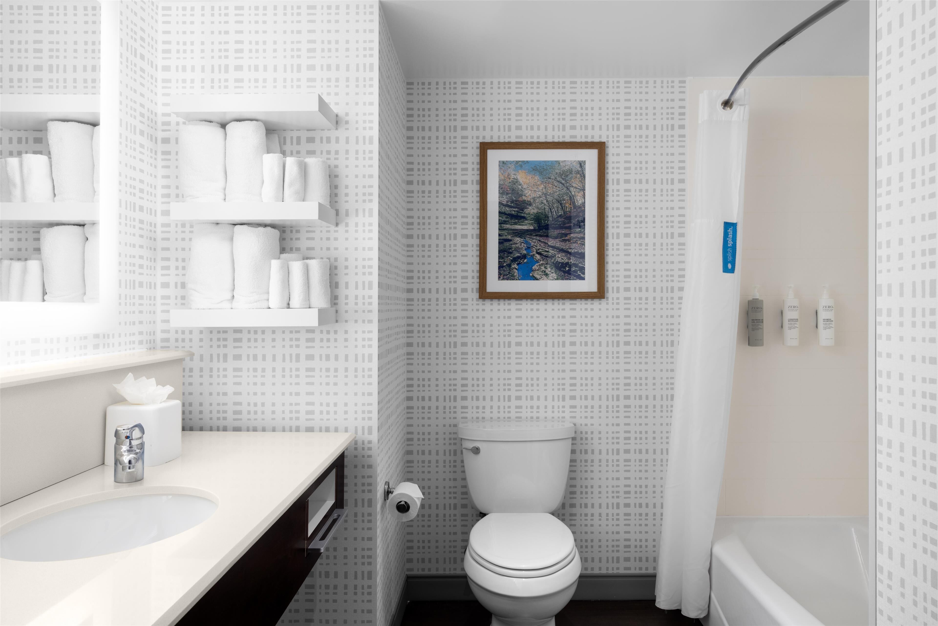 Une salle de bain équipée de toilettes, d’un lavabo et d’étagères où sont rangés les articles de toilette.
