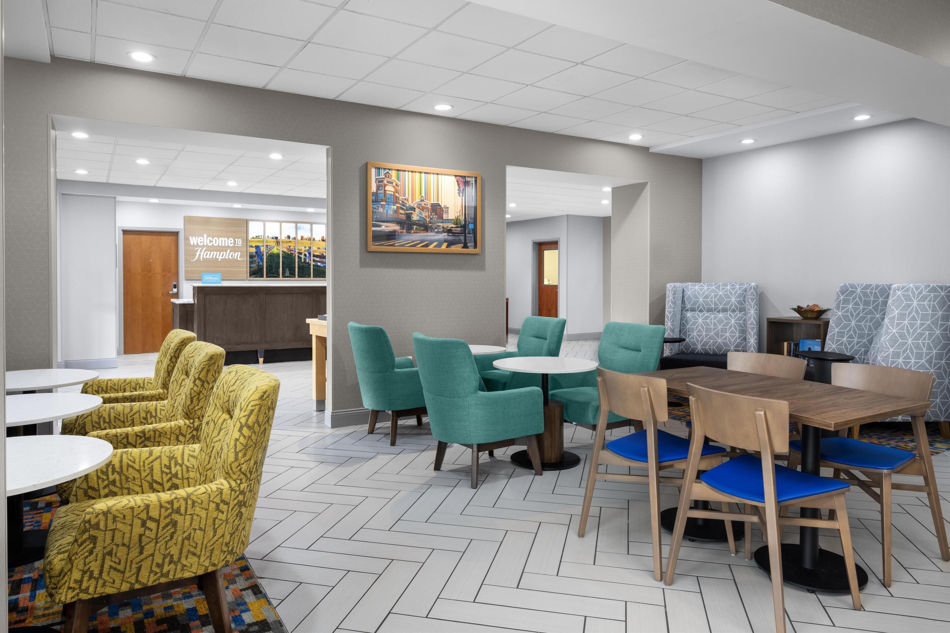 A hotel lobby with a reception desk, seating areas with patterned chairs, and a painting on the wall.